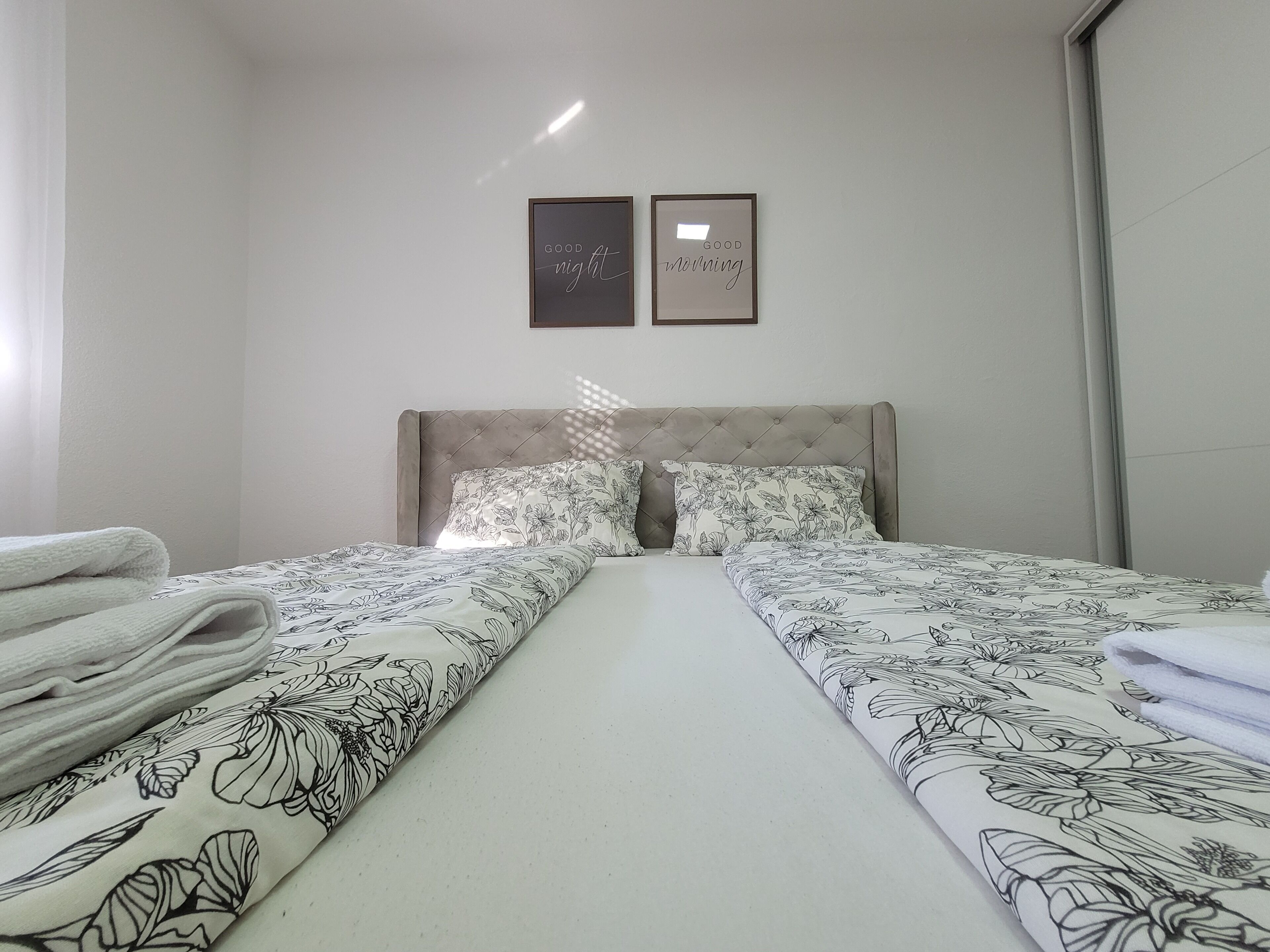 A hotel room with two beds, a headboard, and two framed pictures on the wall.