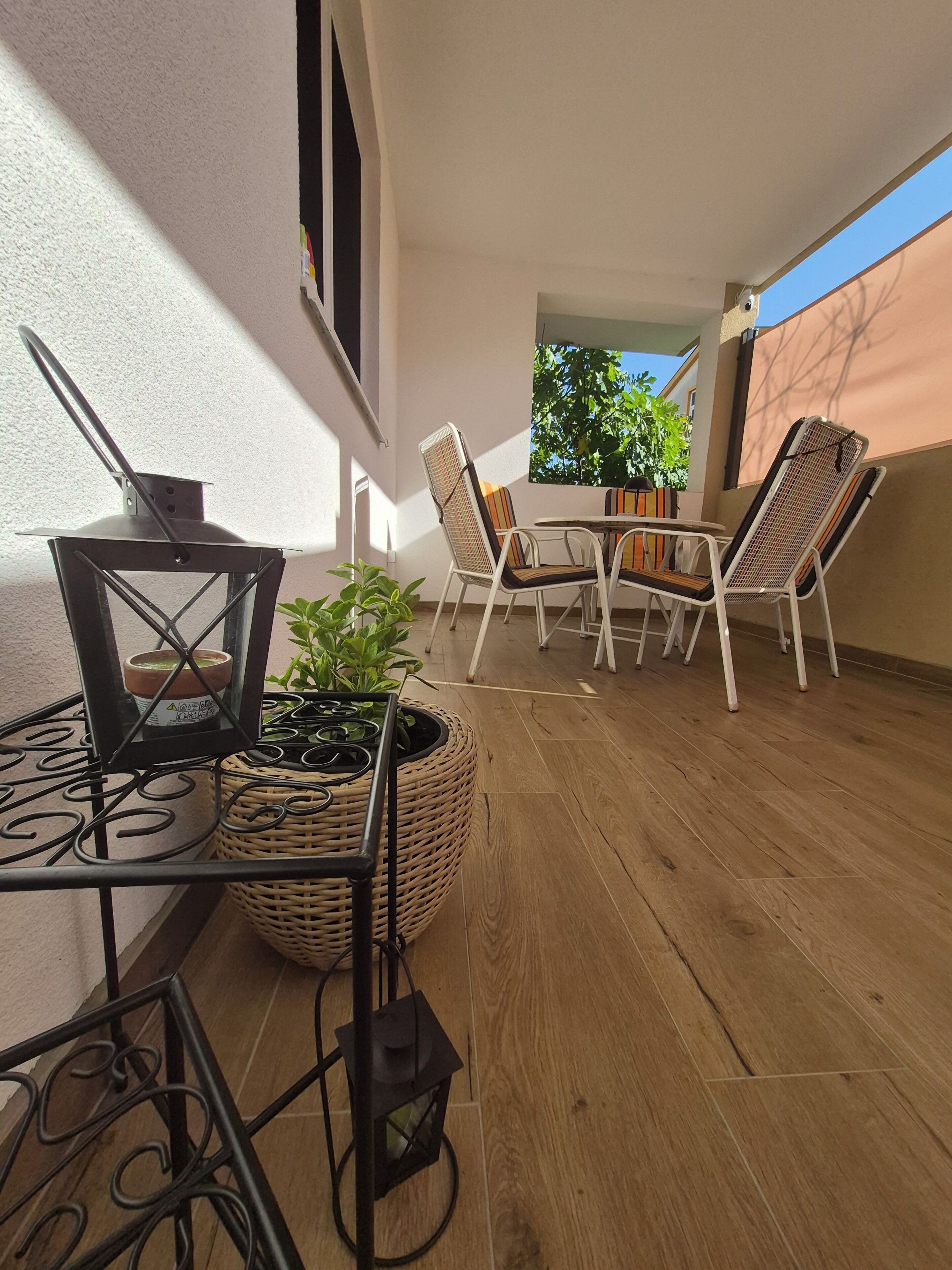 A balcony with a table and chairs, a potted plant, and a hanging lantern.