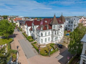 A large, historic building with a prominent tower and multiple windows, surrounded by a paved street and greenery. - Holiday Apartment With 1 Bedroom (Heringsdorf)