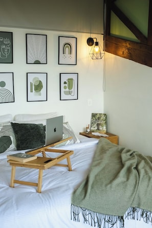 A bedroom with a bed, a laptop, a bedside table with a book, and wall art.