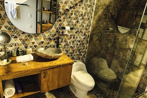 A bathroom with a wooden vanity, a round sink, a mirror, a toilet, and a shower area with a glass door.