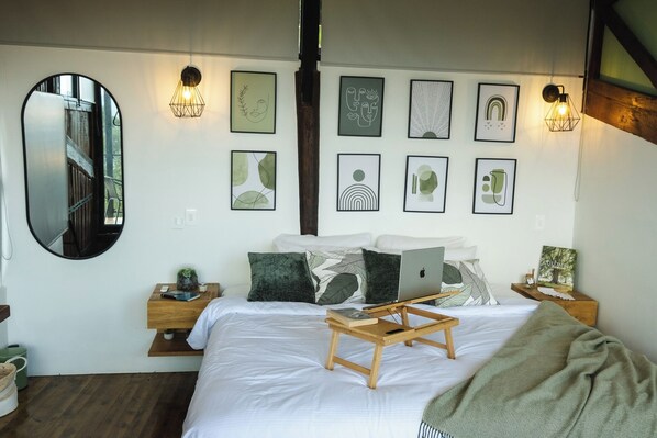 Un dormitorio con cama, mesitas de noche, una computadora portátil y una obra de arte en la pared.