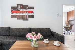 A living room with a dark gray sofa, a wooden coffee table, a vase with pink roses, and a floral teacup and saucer. - Modern 2BR Apartment in Central Limassol – Comfort & Convenience (Lemesos)