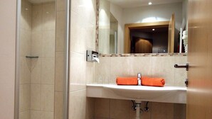 Ein Badezimmer mit einer Duschkabine, einem Waschbecken mit Handtuch und einem Mülleimer.