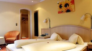 Ein Hotelzimmer mit Doppelbett, einem Sessel, einem Nachttisch und einem Sonnenblumenbild an der Wand.