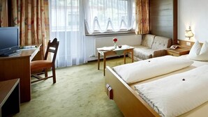 Ein Hotelzimmer mit Bett, Schreibtisch, Sessel, Sofa und Fernseher.