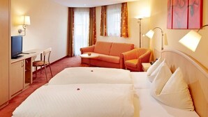 Ein Hotelzimmer mit zwei Betten, einem Schreibtisch mit Computer, einer Couch und einem Fernseher.