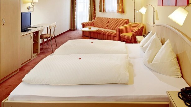 Ein Hotelzimmer mit einem Bett, einem Schreibtisch, einem Sessel, einer Couch und einem Fernseher.