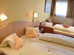 A hotel room with two beds, a bedside table, a lamp, a radiator, and a window with curtains. - Shared Rooms in the Main Building - Landhotel Kaserer (Bramberg am Wildkogel)