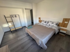A bedroom with a bed, a wooden floor, a ladder, and a wall-mounted shelf.