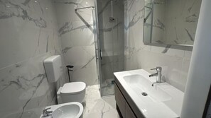 Un baño moderno con ducha envuelta en vidrio, inodoro blanco y un lavamanos grande con espejo sobre él.