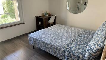 Une chambre à coucher avec un lit, un bureau, une chaise, un miroir rond et une fenêtre.