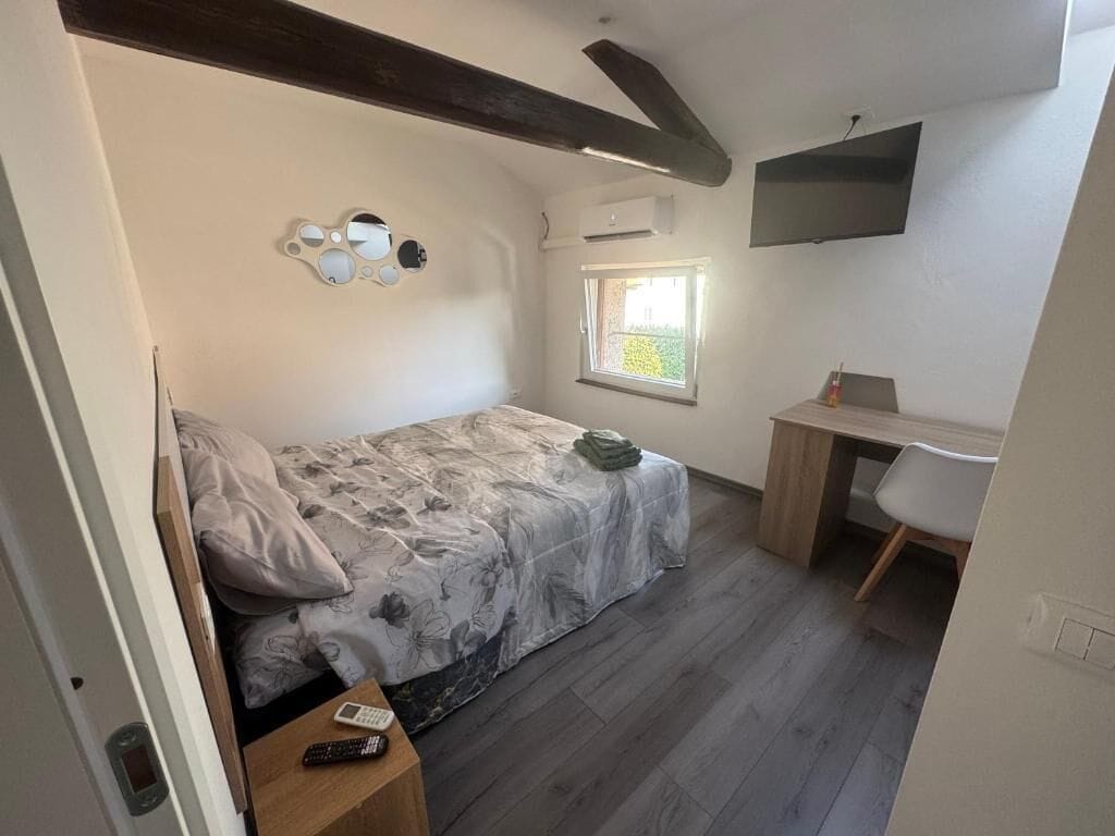 Ein Schlafzimmer mit einem Bett, einem Schreibtisch, einem Sessel, einem Fenster und einem an der Wand befestigten Fernseher.