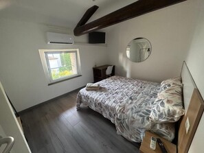Une chambre à coucher comprenant un lit, une table de chevet, un miroir, une fenêtre et un appareil de climatisation.