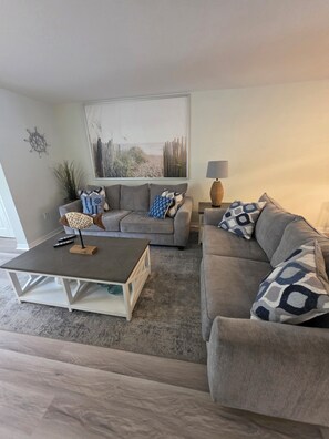 Un salon avec un canapé gris, une table basse et un tableau accroché au mur.