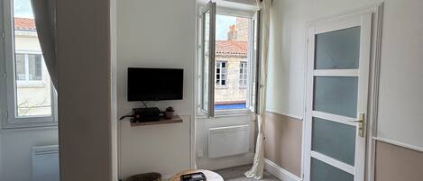 A room with a bed, a television on the wall, a small table, and a window with curtains.