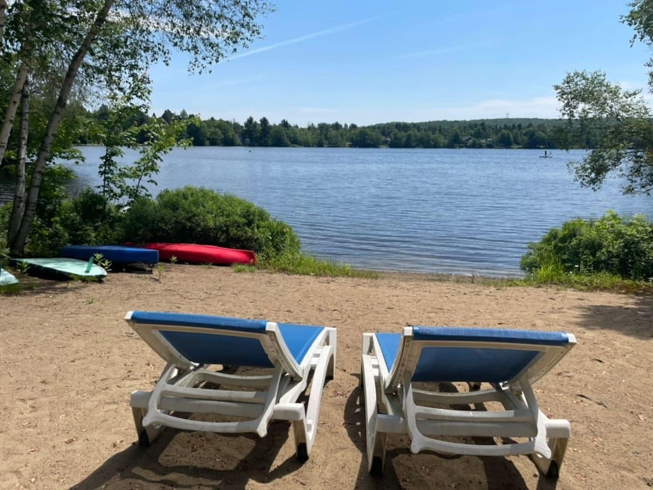 Two beach chairs facing a lake with boats and greenery in the background.