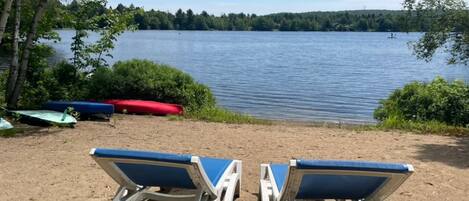 Two beach chairs facing a lake with boats and greenery in the background.
