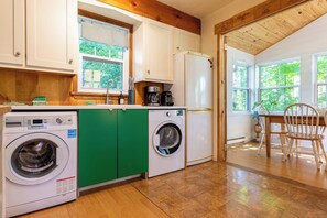 A compact kitchen with a washing machine, a coffee maker, and a refrigerator. - KazaLutins | Plage privée | Petit coin de paradis (Saint-Élie-de-Caxton)