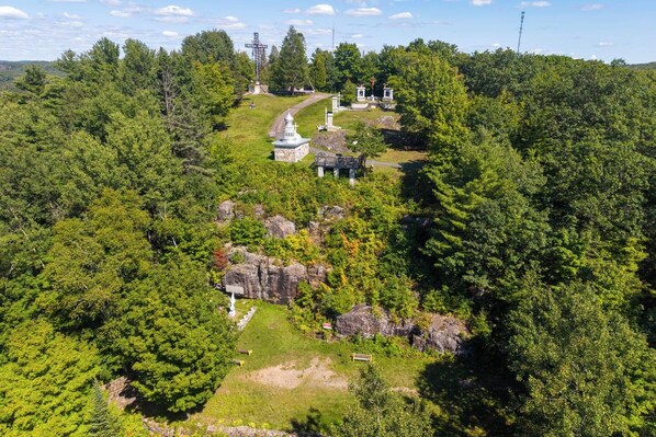 A forested area with a pathway leading to a white building with a dome roof, surrounded by trees and rocks. - KazaLutins | Plage privée | Petit coin de paradis (Saint-Élie-de-Caxton)