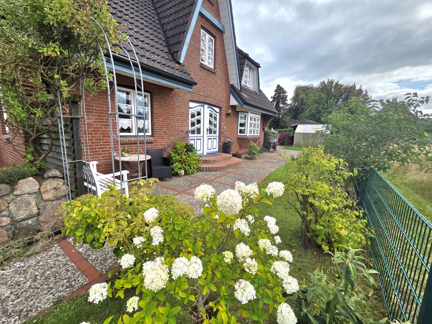 A two-story house with a brick exterior, a front porch, and a garden with white flowers.