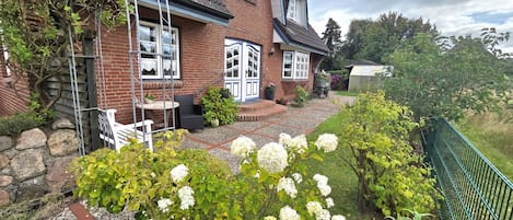 A two-story house with a brick exterior, a front porch, and a garden with white flowers.