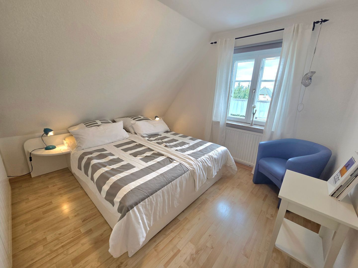 Et soveværelse med seng, natbord, lampe, stol og vindue.
