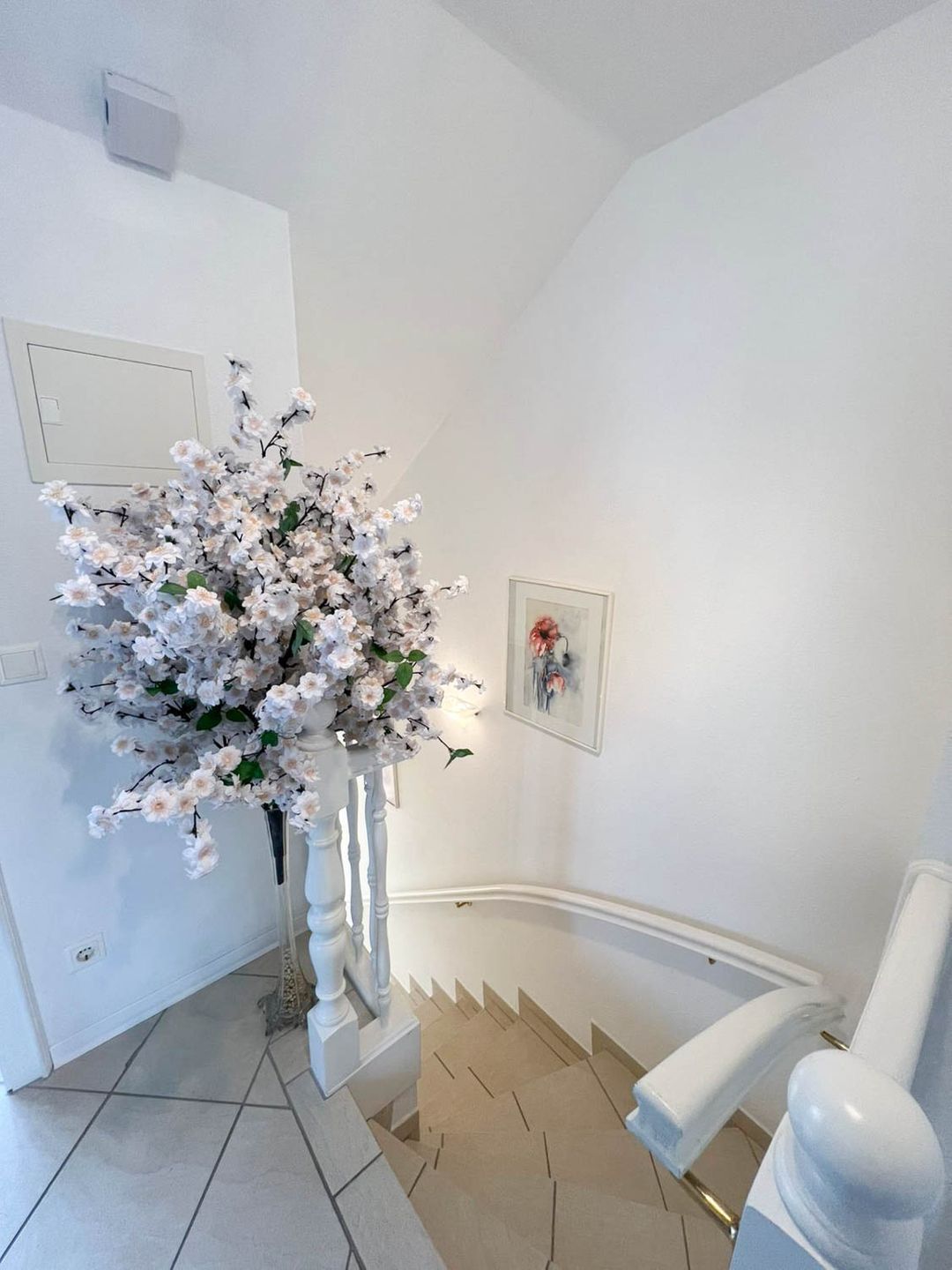 A staircase with a white railing, a white wall, and a framed picture on the wall.