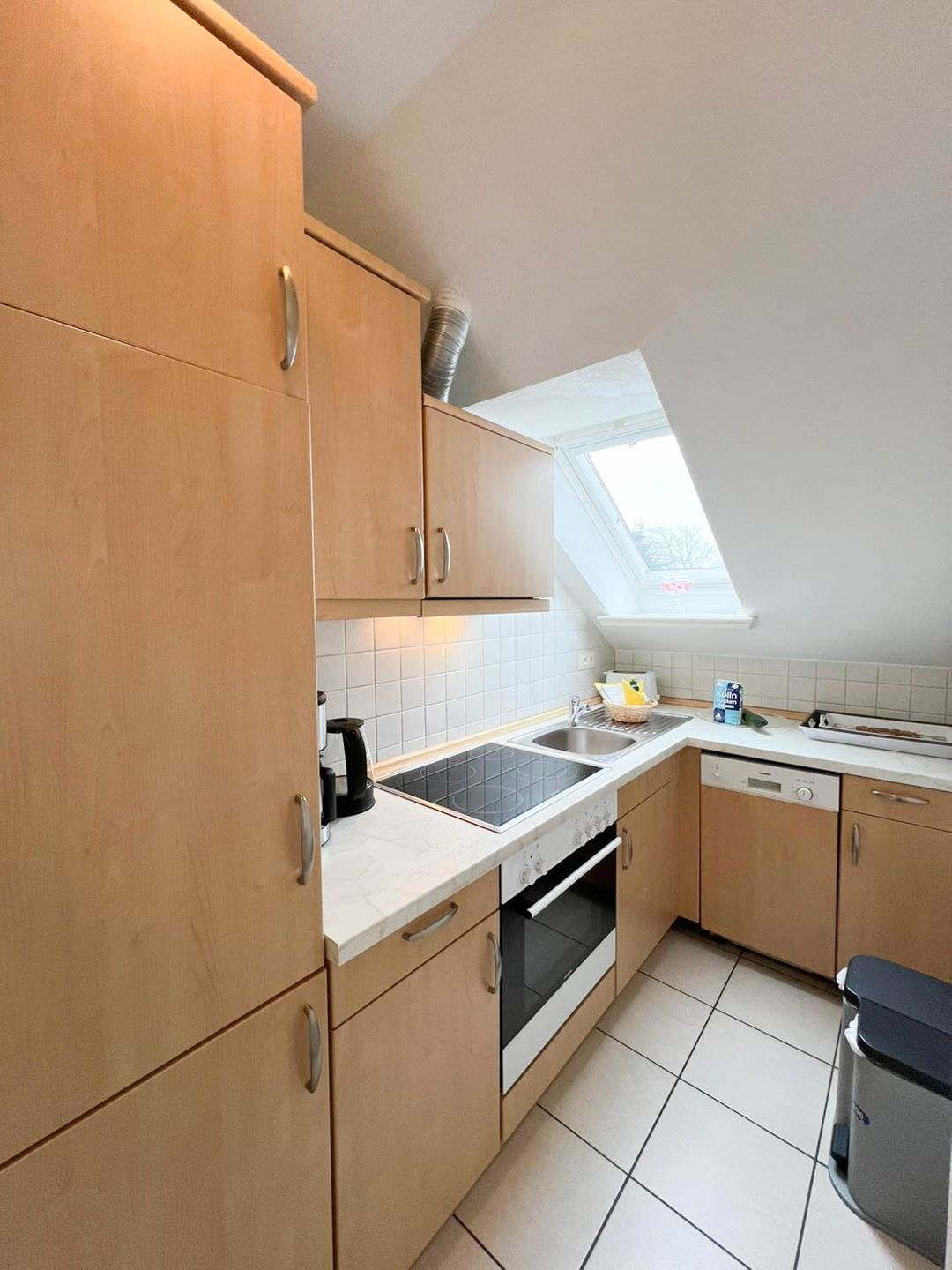 A modern kitchen with wooden cabinets, a built-in oven, a dishwasher, and a skylight.
