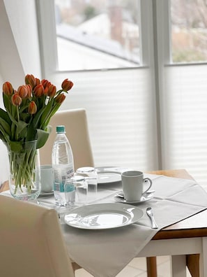A dining table set with plates, cutlery, a glass, a bottle of water, and a vase with tulips. - Leyla OG - Leyla Vacation Rental on Sylt: Balcony, Parking, and Dog-Friendly (Sylt)