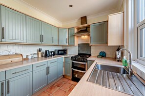 A modern kitchen with light blue cabinets, a stainless steel sink, and a gas stove. - Host & Stay | House On The Hill (Hastings)