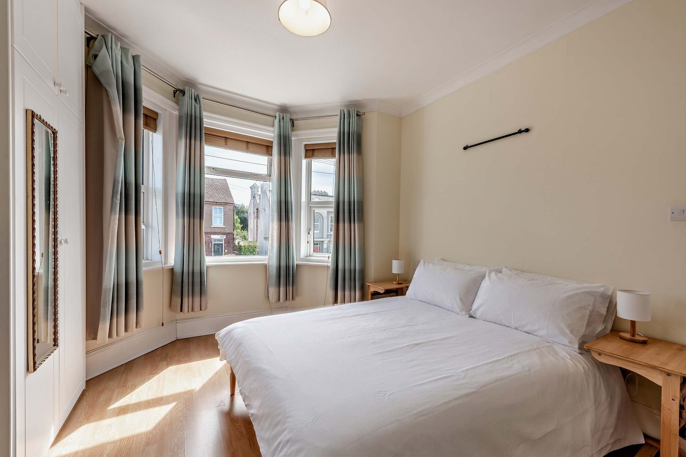 Ein Schlafzimmer mit einem großen Bett, zwei Nachttischen, einem Spiegel und Blick ins Freie.
