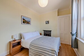 A bedroom with a bed, bedside table, lamp, framed pictures, a fireplace, and a door. - Host & Stay | House On The Hill (Hastings)