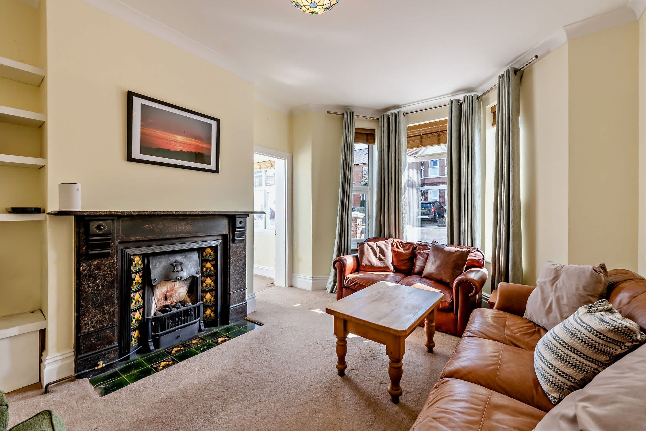A living room with a fireplace, leather sofa, and a painting on the wall.