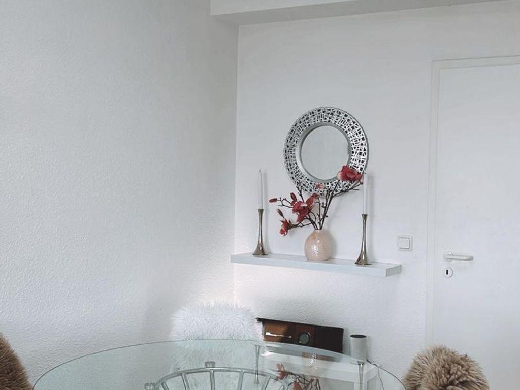Ein Zimmer mit einem Glastisch, einer weißen Tür und einem dekorativen Spiegel an der Wand.