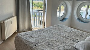 Ein Schlafzimmer mit einem großen Bett, einem Fenster mit Vorhängen, einem Heizkörper und Blick ins Freie.