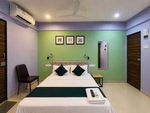 Habitación de hotel con cama, una silla, escritorio y ventilador de techo.