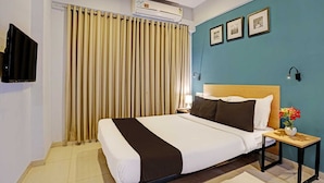 A hotel room with a bed, a nightstand, a lamp, a wall-mounted TV, and a ceiling fan. - Deluxe Bhumi Stay inn (Bhiwandi)