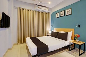 Une chambre d’hôtel équipée d’un lit, d’une table de chevet, d’une lampe, d’un téléviseur fixé au mur et d’un ventilateur de plafond.