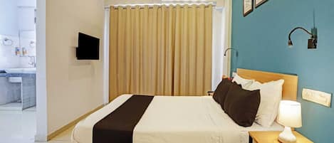 A hotel room with a bed, bedside table, lamp, and a bathroom visible in the background.