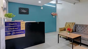 A reception desk with a 'Check-in' sign, a 'Check-out' sign, and a 'No Smoking' sign.