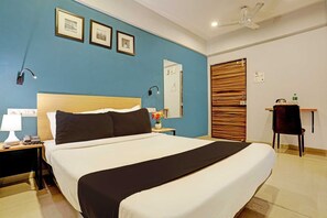 Une chambre d’hôtel avec un grand lit, une table de chevet avec une lampe, un bureau avec une chaise et une porte en bois.