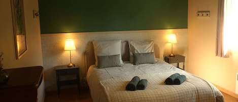 Un dormitorio con una cama, dos mesitas de noche, una lámpara colgante y una ventana con cortinas.