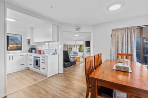 Una cocina moderna con armarios blancos, un comedor con mesa de madera y una sala de estar con sofá y televisor.