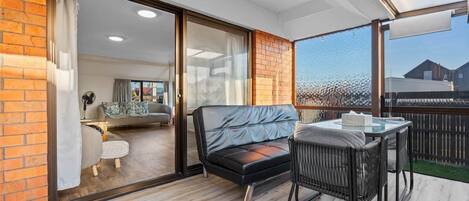 A balcony with a sofa, a table, and chairs, and a view of a building in the background.