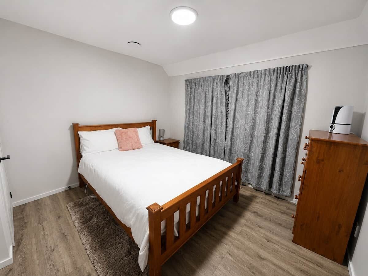 Een slaapkamer met een houten bed, een nachtkastje, een kledingkast en een grijs gordijn.