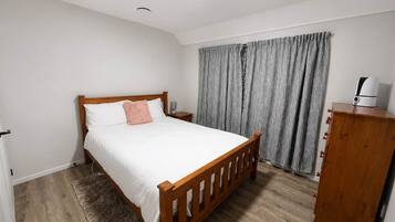 Een slaapkamer met een houten bed, een nachtkastje, een kledingkast en een grijs gordijn.