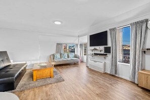 A modern living room with a sofa, a coffee table, a flat-screen TV, and a large window with curtains. - Relaxing Dunedin City Escape (Dunedin)