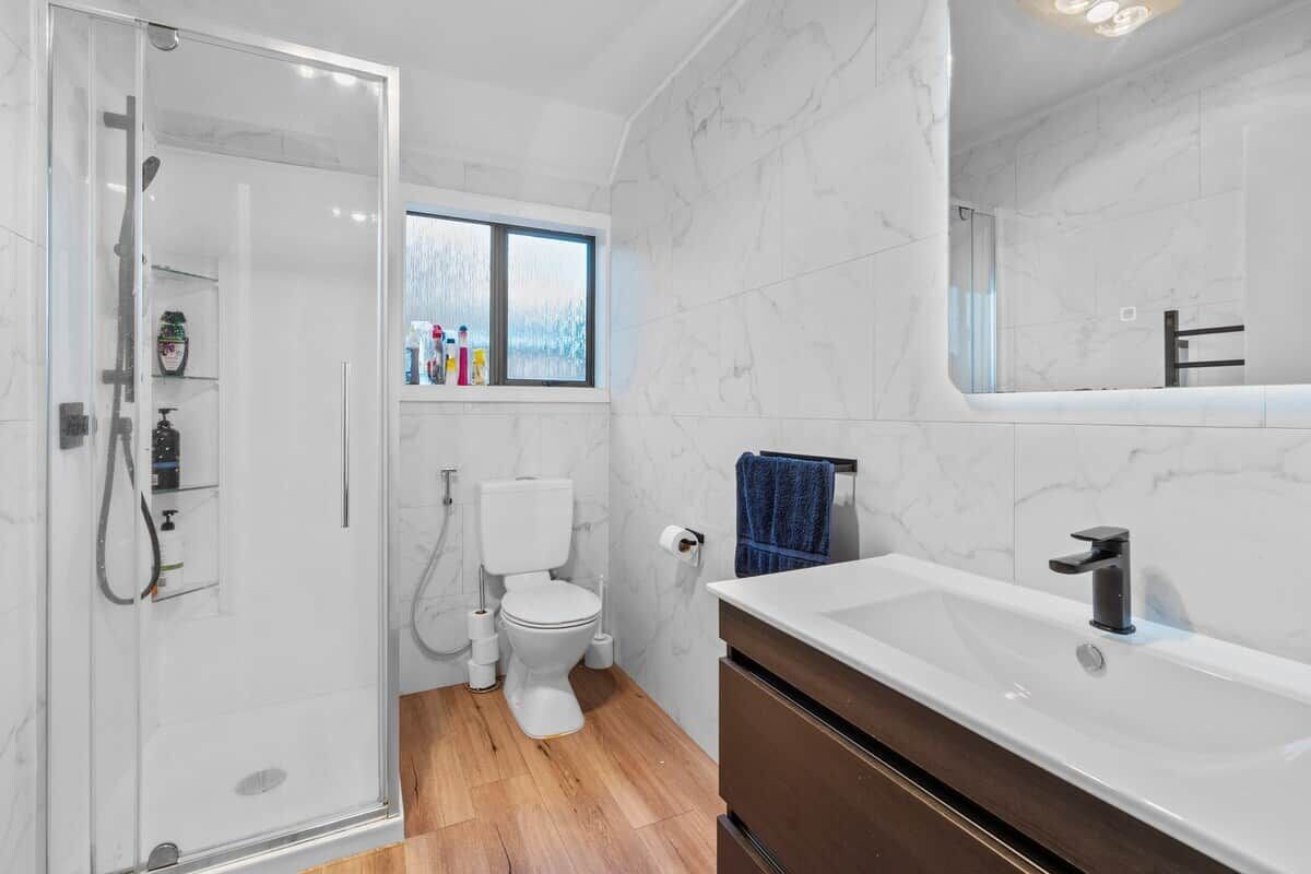 A modern bathroom with a glass shower enclosure, a white toilet, a large bathtub, and a window providing natural light.