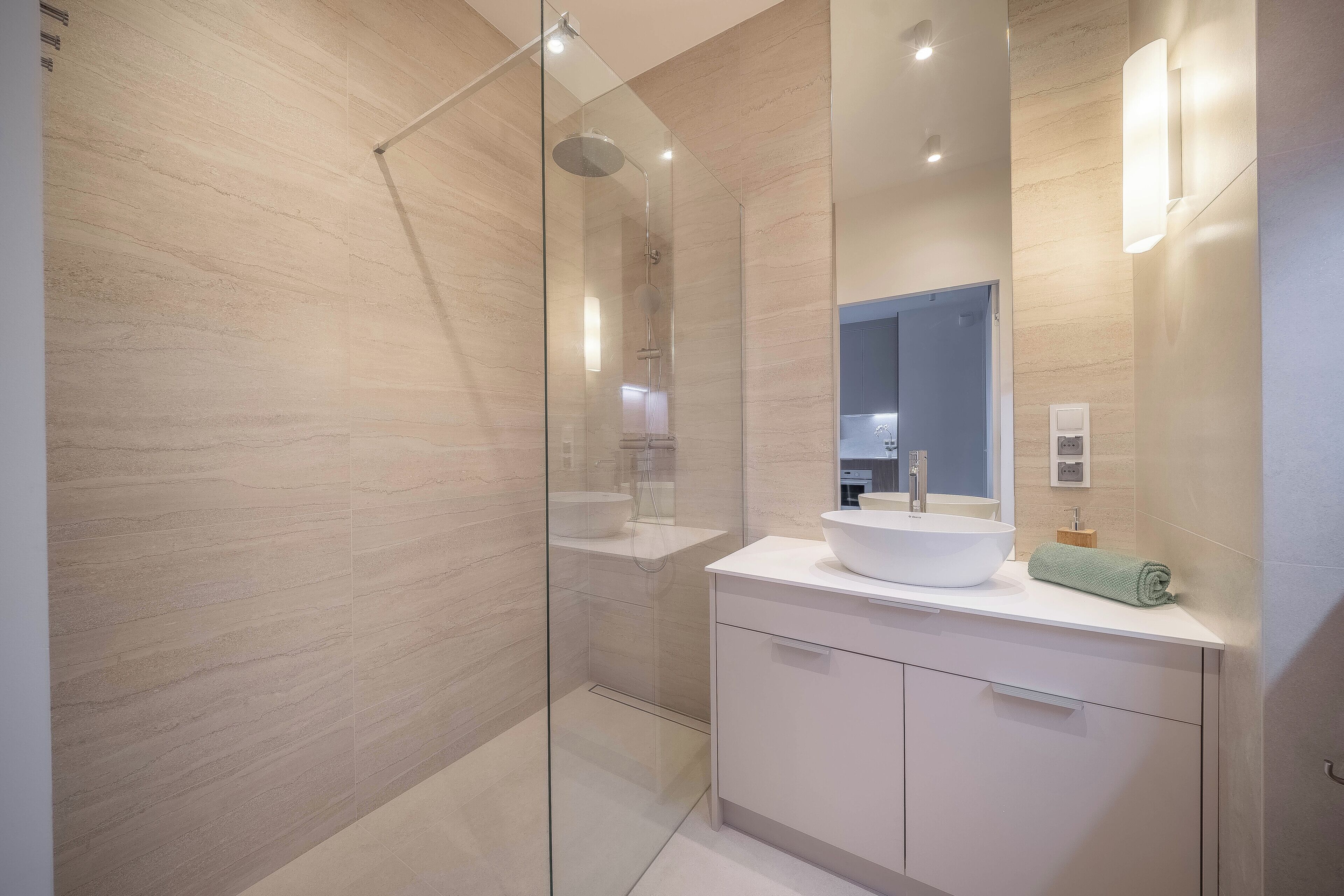 Un baño moderno con cabina de ducha de vidrio, un lavabo blanco y un espejo grande.